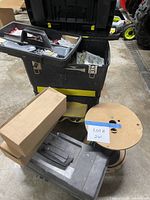 Rolling toolbox open with tray of small electrical parts, cardboard box, hard case, cable spool visible