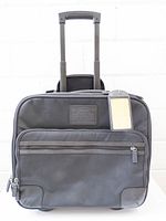 Front view of Coach ballistic nylon carry-on roller with handle extended and ID tag visible