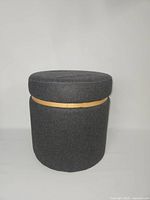 Front view of dark gray round storage ottoman with lid in place