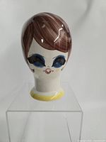 Front view of glazed ceramic hat stand head showing facial decoration and yellow base trim