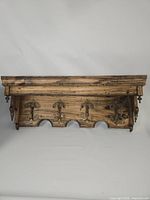 Front view of wood shelf with three brass hooks and scalloped edge