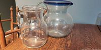 Two glass pitchers on wooden surface; shows size and style differences