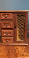 Front of wooden jewelry box, drawers and mesh door visible