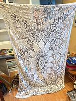 Full view of rectangular ivory lace tablecloth held up to show overall size and pattern
