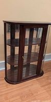 Front view of dark wood display cabinet with glass door and curved glass sides