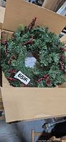 Wreath in box, showing full view of faux greenery, pinecones, berries
