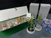 Open green presentation box with 12 wrapped egg ornaments; two glass Christmas tree figurines and bag of mini ornaments
