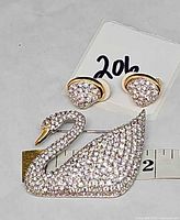 Swarovski swan brooch with matching clip earrings beside measuring tape