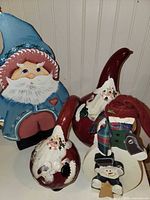 Group view of wooden Santa, two red gourd Santas, wooden snowman