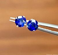 Front view of sapphire stud earrings held by tweezers showing color and cut