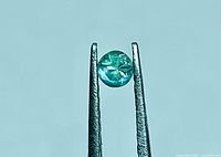 Round alexandrite held in tweezers, showing bluish-green color