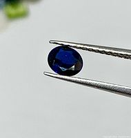 Faceted oval blue sapphire held by tweezers, top view