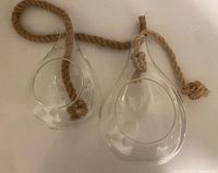 Two clear glass teardrop planters with rope hangers side by side