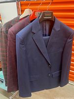 Three suits hanging: navy front, burgundy plaid middle, grey back
