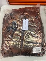 Sealed plastic package containing metallic puffer ski suit with tags