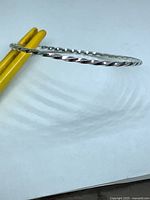 Side view of thin silver-tone twisted bangle held by yellow tool
