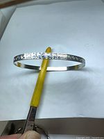 Full view of silver-tone bangle resting on tool showing exterior pattern