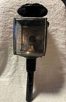 Front view of black metal carriage lamp showing beveled glass lens and mounting stem
