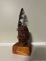 Front view of carved wooden warrior bust on base with feather