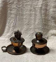 Both small copper finish oil lamps side by side showing overall design and glass chimneys