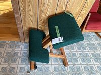Side view showing wood frame, green upholstered seat and knee pad, and casters