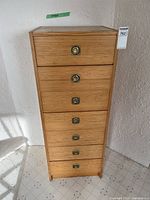 Front view showing full height, seven drawers, brass pulls, light wood finish