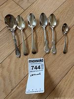 Six sterling spoons laid out on wood floor with lot card