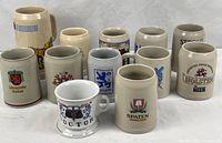 All twelve stoneware beer mugs grouped, front graphics visible