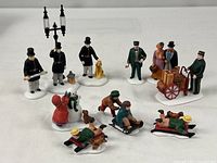 Group shot of all figurines including constables with lamp, travelers with luggage cart, and sledding children