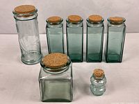 Seven green glass jars with cork lids displayed together