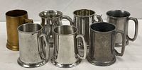 Group shot of seven metal beer mugs/tankards showing materials and variety