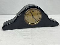 Front view of black camelback mantel clock with brass bezel and gold dial