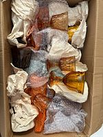 Box containing multiple amber pressed glass stemmed goblets wrapped in packing material