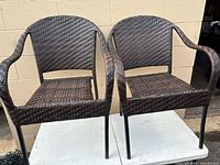 Front view of two woven resin patio armchairs on metal legs
