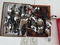 Two boxes filled with over 50 pieces of flatware showing black swirl handles and stainless heads