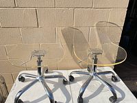 Two clear acrylic swivel chairs on table showing full view with bases and casters