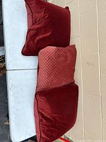 Three square burgundy pillows on table, two plain velvet and one textured