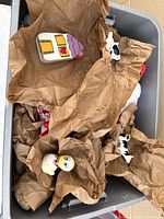 Large plastic tote containing wrapped salt and pepper shakers; visible house-shaped shaker, cow figurine, cartoon head shaker