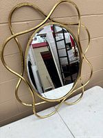 Front view of oval gold looping frame mirror leaning against wall
