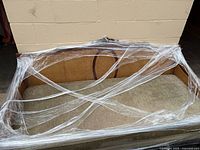 Overall view of settee wrapped in plastic showing cane back and upholstered seat