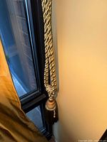 Close view of one braided rope tieback hanging on curtain, showing tassel and bead accents