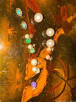 Multiple stud earrings laid out on lacquered surface showing sizes and colours