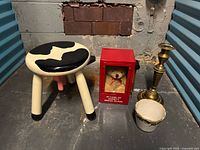 All four items grouped: cow-pattern stool, red teddy bear case, brass candlestick, porcelain cachepot