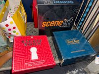 Three boxed board games on shelf: Scene It? black box, Escape Room red box, Trivial Pursuit blue box