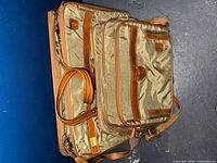 Folded garment bag and carry-on bag stacked together showing leather trim and overall wear