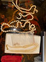 Boxed pearl necklace with gold-tone clasp and two additional pearl strands on lacquered surface
