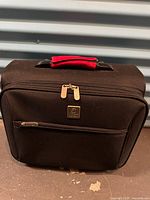 Front view of Newell carry-on bag showing front pocket, logo plaque, red handle