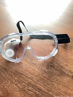 Unpackaged clear safety goggle showing lens, vent and strap