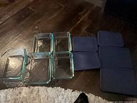 Five clear rectangular glass containers arranged on floor next to matching dark blue lids