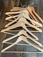 Nine wooden hangers layered on dark wood surface